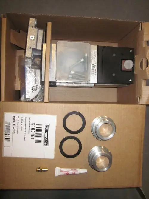 Gasblock mit mehreren Metallteilen, Dichtungen und Montagezubehör in einem Karton, Marke Remeha. Verpackt für den Einsatz in Heizsystemen.